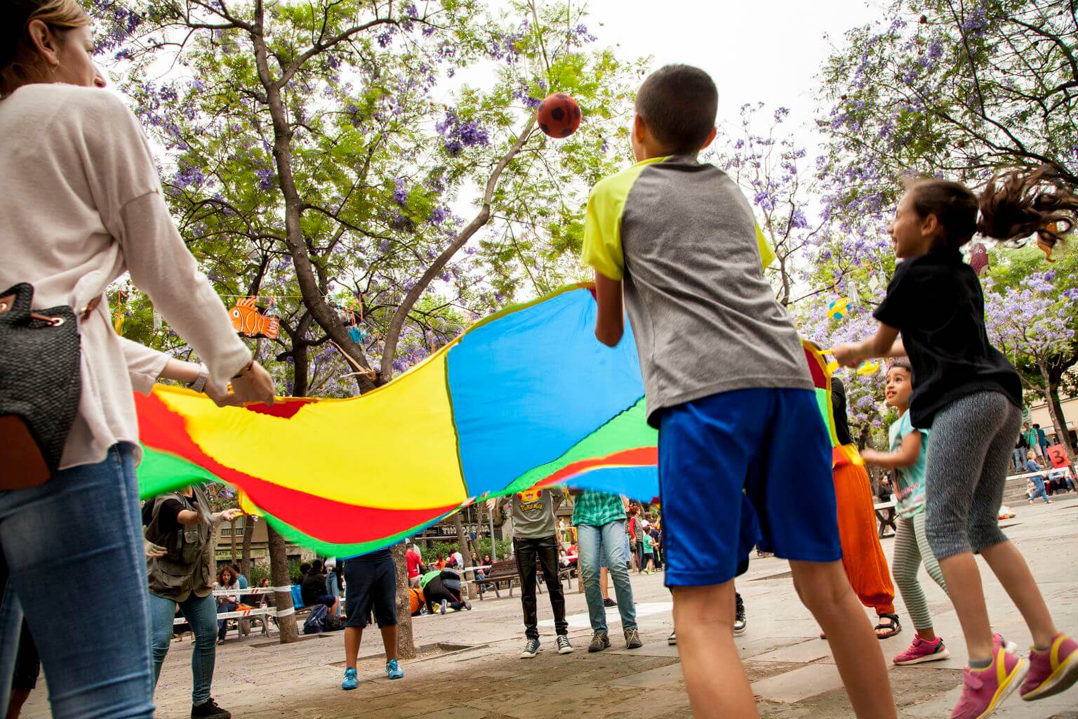 Uns nens jugant amb una tela de colors que fa volar una pilota. <span>Carlota Serarols</span>